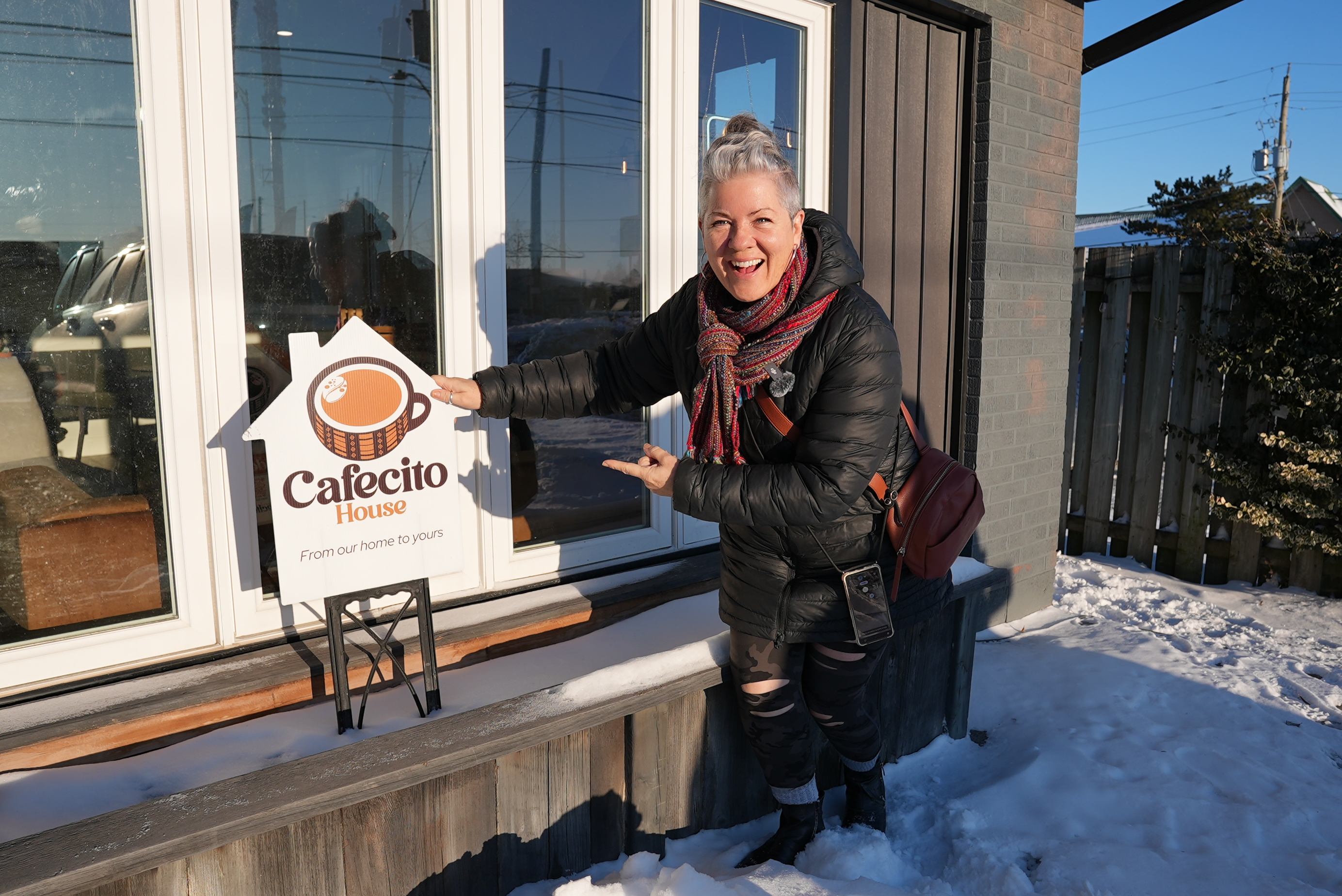 A woman smiles in front of a coffee shop window pointing to the sign