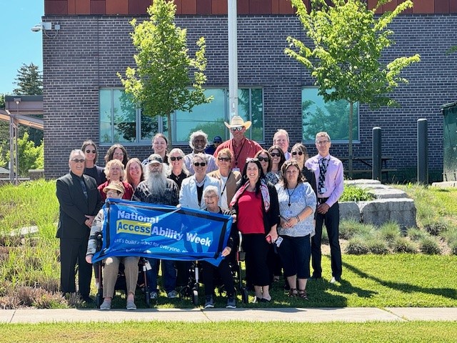 Members of the Accessibility Advisory Committee, Haldimand staff and Council pose in front of the National AccessAbility Week flag.