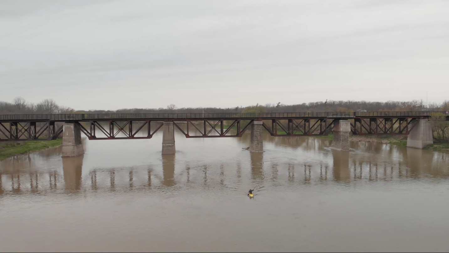 An old railway bridge over the river with a kayaker going under