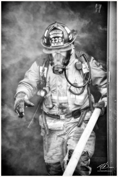 A firefighter emerges from a burning building; wisps of smoke clutching at him