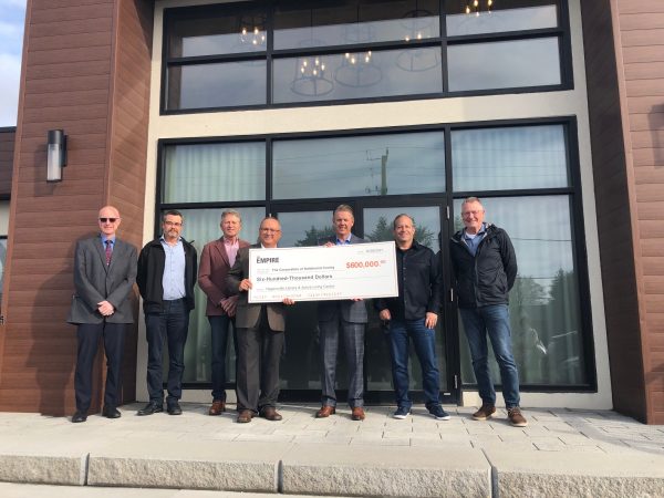 Members of Haldimand Council, Haldimand staff, community members and Empire representatives pose atop a set of stairs outdoors with a ceremonial cheque for $600,000.